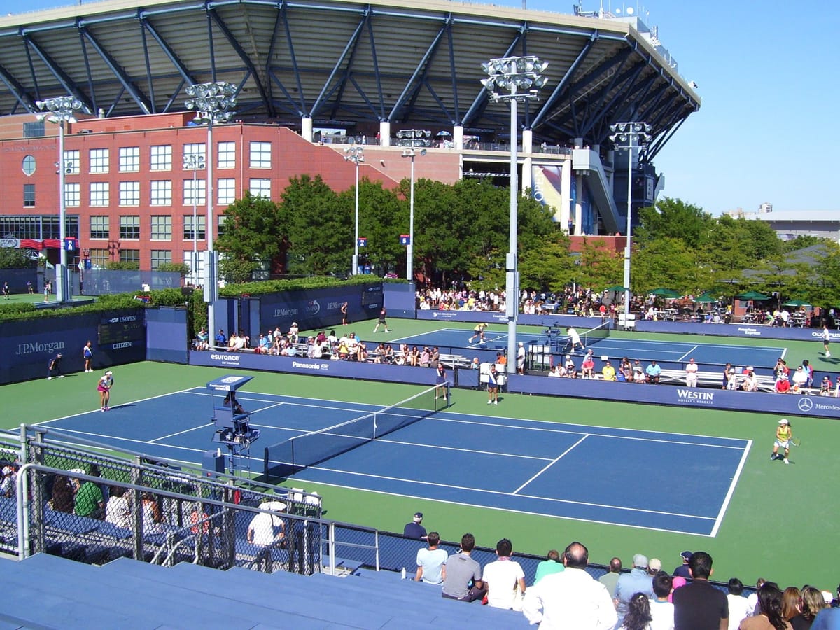 Historical 2010 view of a US Open qualifying match on an outer court at the USTA Billie Jean King National Tennis Center, with Arthur Ashe Stadium behind.